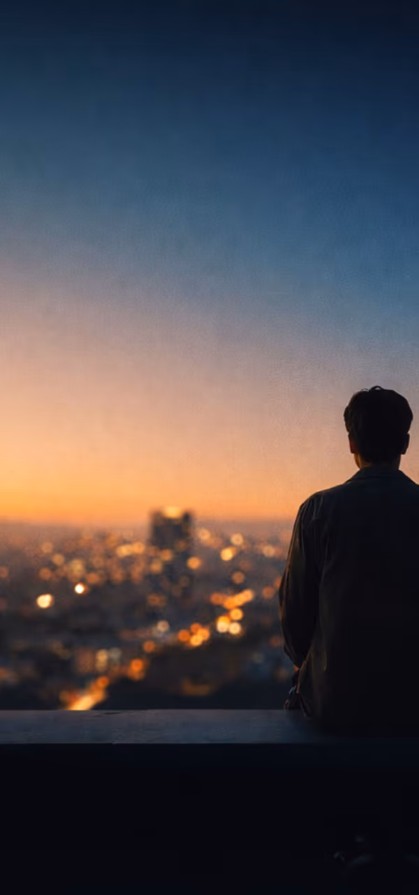 A person sitting above a city lit up at dusk.